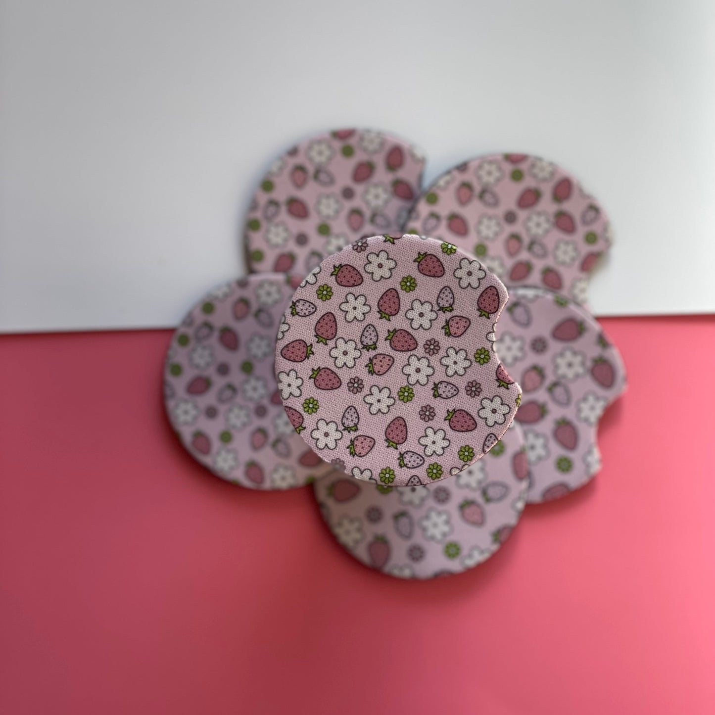A set of pink and white floral patterned car coasters designed to fit in car cup holders.