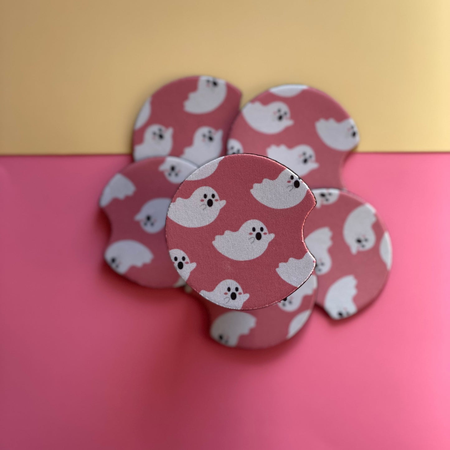 A set of pink and white coasters with a ghost pattern, designed to fit in car cup holders.